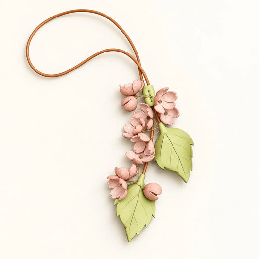 Cherry Blossom Cascade bag charm with blush pink flower clusters, two pale green leaves, and a brown cord loop on an ivory background.