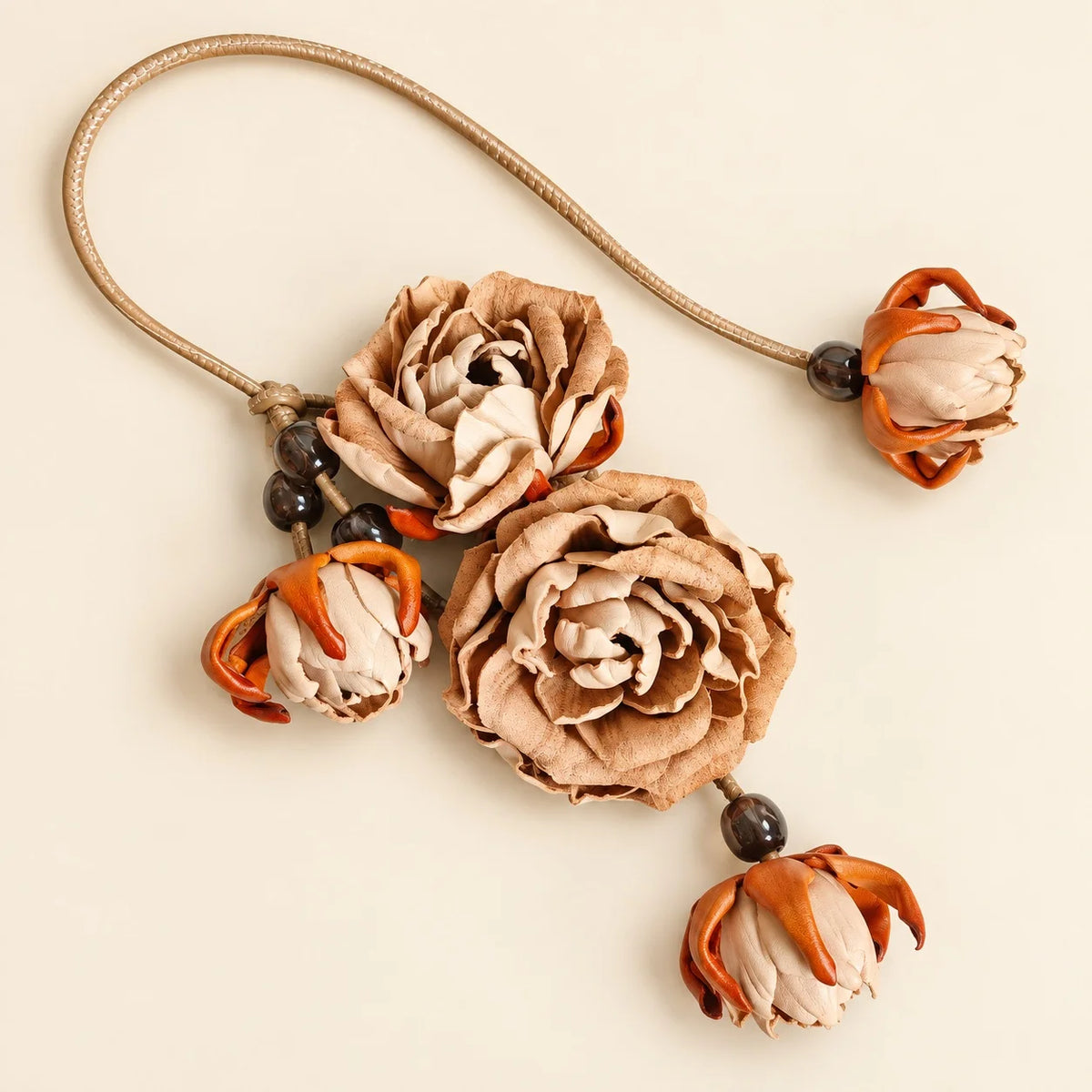 Handcrafted beige cowhide leather rose bag charm with two sculpted blooms, cream buds, orange accents, and a long leather cord on an ivory background.