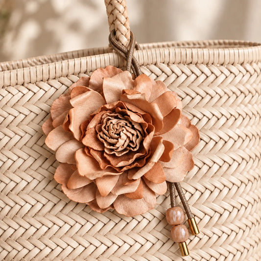Large natural tan sculpted leather peony bag charm displayed on a woven neutral tote with layered handcrafted petals