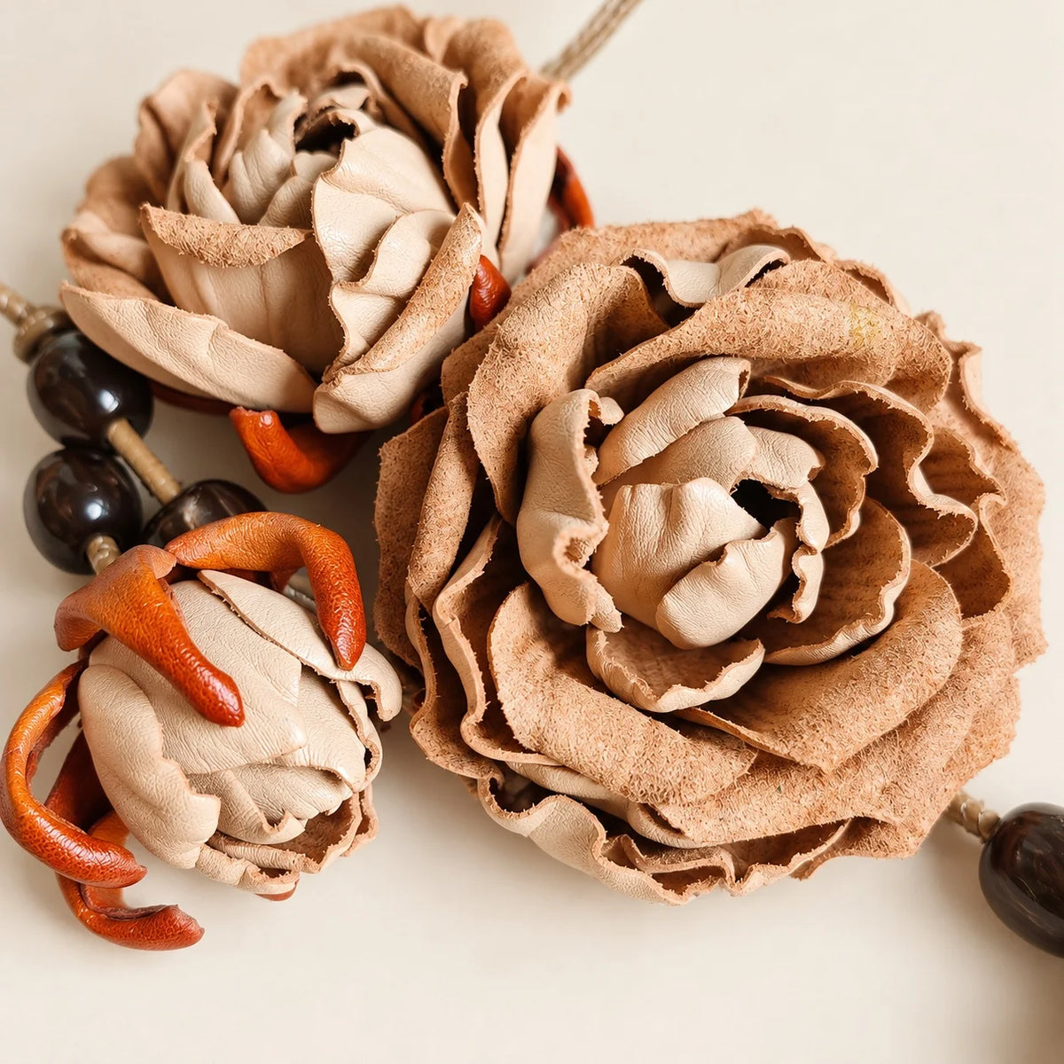 Close-up of handcrafted beige cowhide leather roses showing textured petal edges, layered cream centers, orange floral accents, and dark beads.