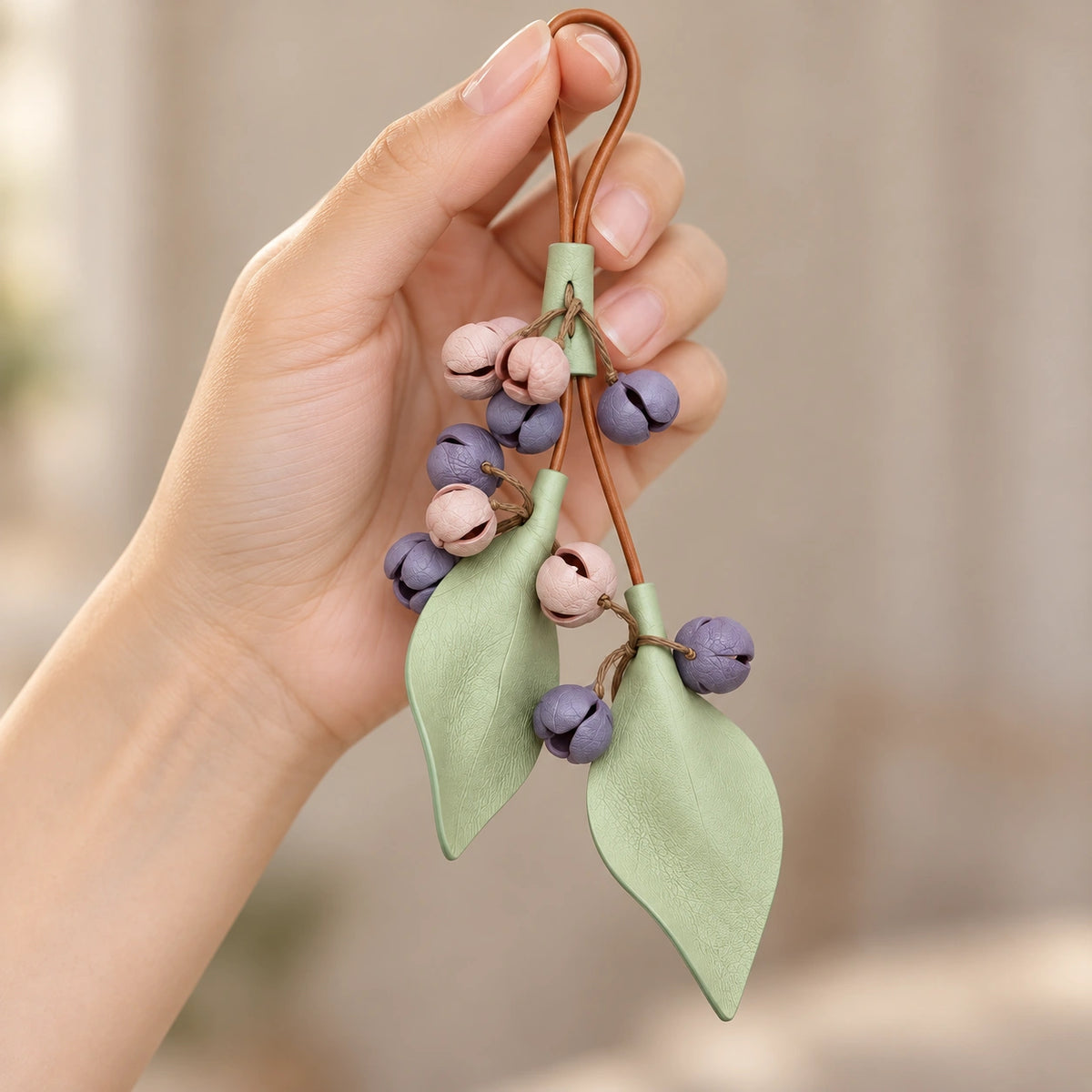 Hand holding a Morandi botanical bud charm showing its brown hanging loop, pastel floral clusters and two textured sage green leaves.
