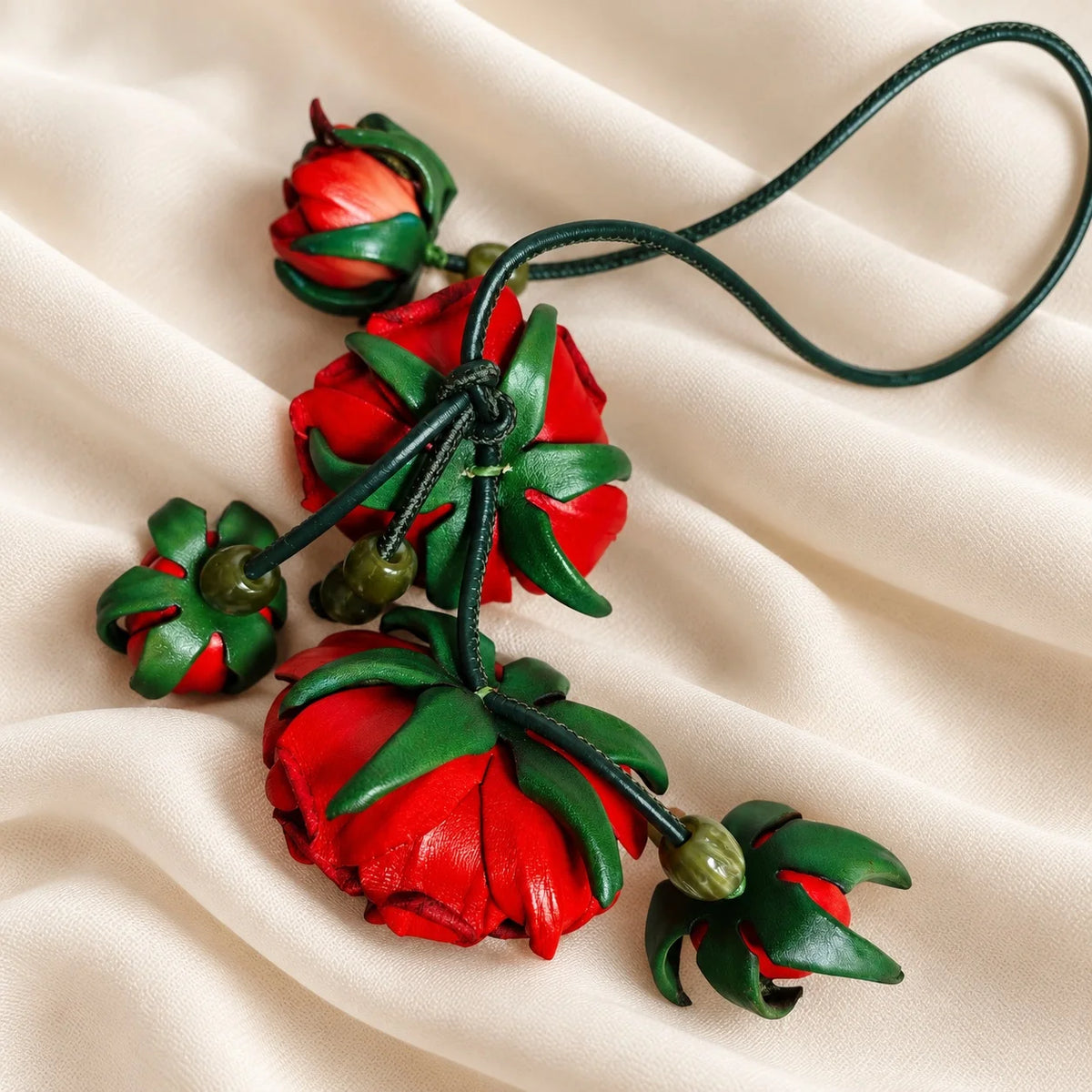 Back view of a crimson red leather rose bag charm showing green leather flower bases, connecting cords, decorative beads, and the hanging loop.