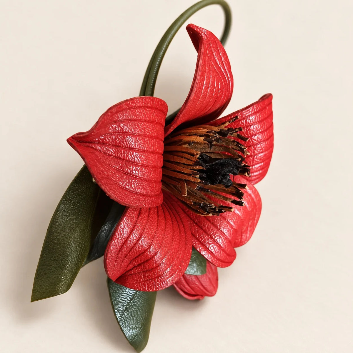 Oblique close-up of the red kapok flower bag charm showing curved petal profiles, a layered dark center and olive green leaves.