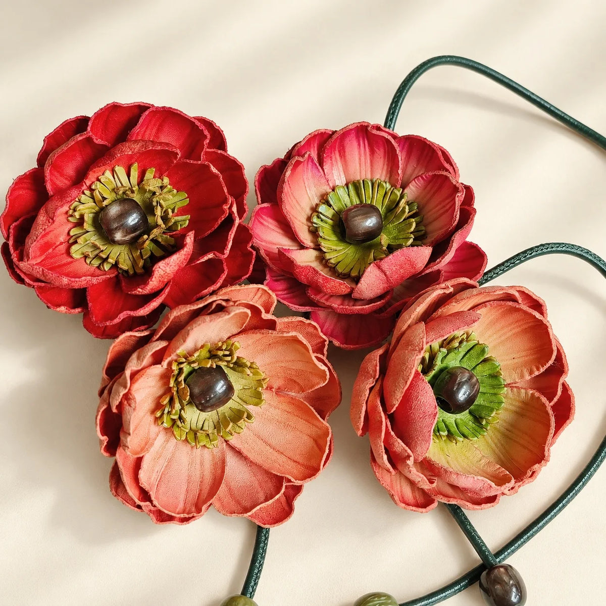 Group detail of four sculpted leather flowers in red, pink and peach shades with layered petals and dark decorative centers.