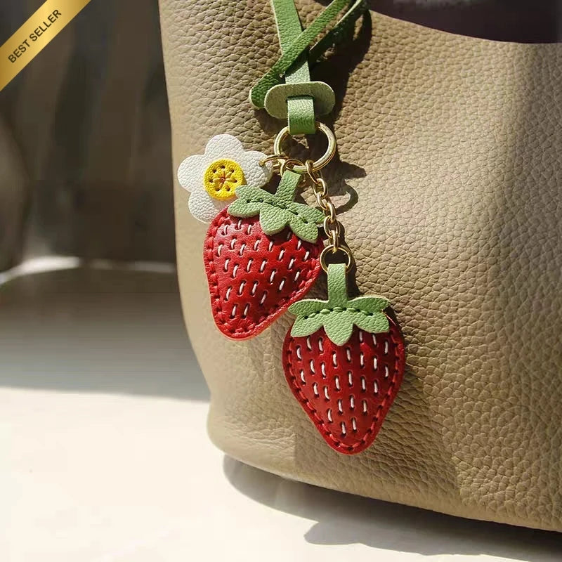 Double strawberry and daisy leather bag charm attached to a warm taupe handbag with gold-tone hardware