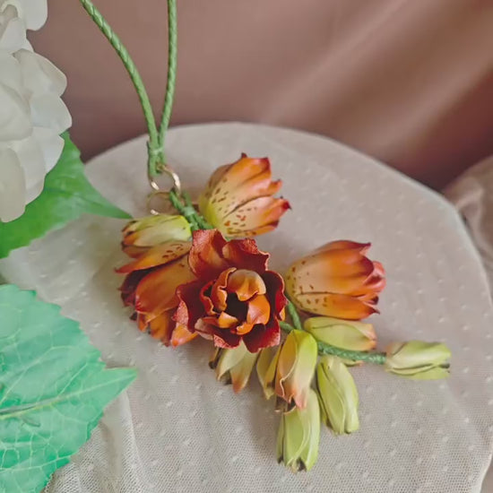 Amber Lily Cascade leather bag charm shown by hand, revealing sculpted orange flowers, green buds and gold-tone clasp.