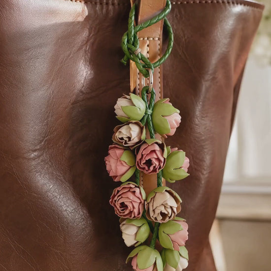 Product video of SHEWEARING Blush Bud Cascade Sculpted Leather Floral Bag Charm, showing pink and cream leather rosebuds, green braided cords and natural movement on a cognac tote.