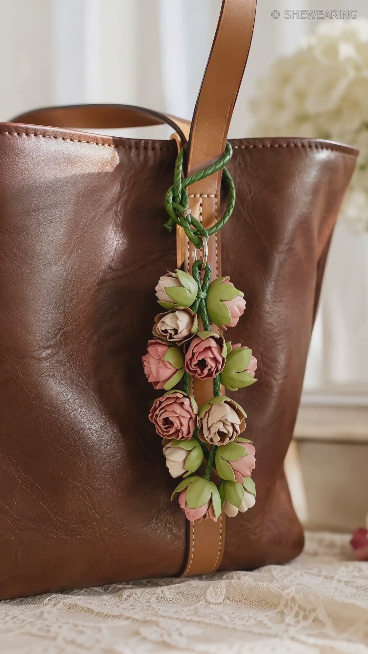 Product video of SHEWEARING Blush Bud Cascade Sculpted Leather Floral Bag Charm, showing pink and cream leather rosebuds, green braided cords and natural movement on a cognac tote.