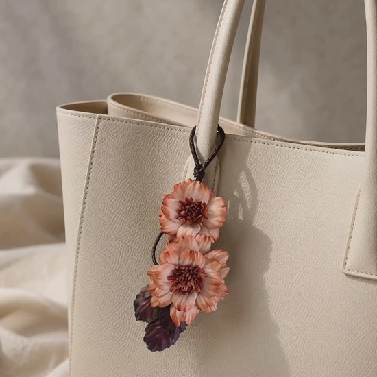 Product video of SHEWEARING Peony Reverie Sculptural Leather Bag Charm, featuring two coral leather peony blooms, textured centers, burgundy leaves and gentle movement on a cream tote.